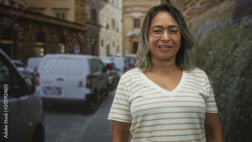 Canvastavla Woman wearing glasses and striped v neck t shirt smiling with eyes closed beside a white van on a narrow cobblestone street with stone buildings; contentment travel memory
