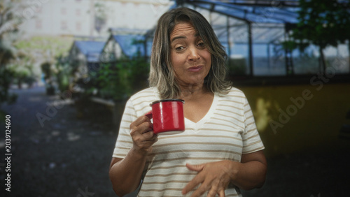 Fotografie Woman holding red cup with hand raised gripping mug in building, grimaces at taste; tasting disgust