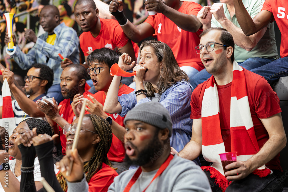 Fototapeta premium Red team football supporter blowing red vuvuzela and cheering in stadium stands during intense soccer match. Sports fans keeping rhythm for team support and football culture.