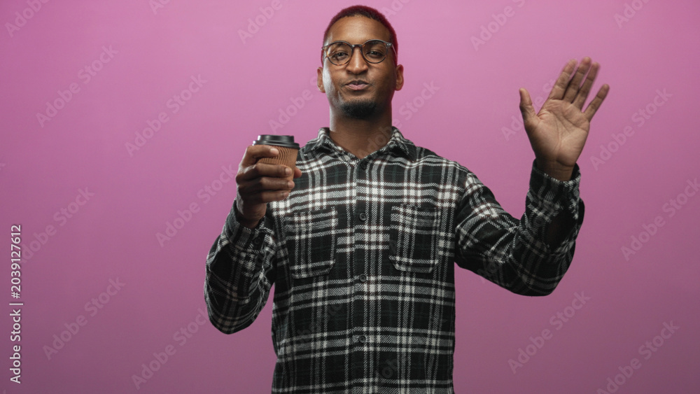 Naklejka premium Man wearing glasses and plaid shirt holding paper coffee cup and waving hand in studio with pink backdrop; friendly greeting.
