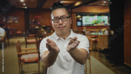 Tableau sur toile Man with glasses and topknot hands open palms up in building restaurant interior facing camera with pleading gesture; confusion