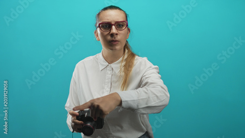 Canvastavla Woman wearing white shirt and red glasses holding dslr camera points finger while speaking in studio; frustration instruction