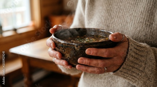 Картината върху платно Person holding a steaming bowl of hearty soup in a rustic setting