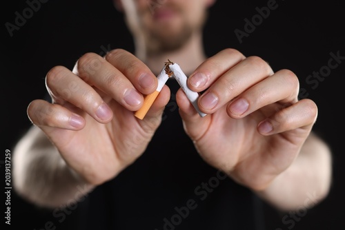 Принти на полотні Man breaking cigarette against black background, closeup