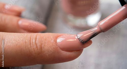 Applying a self-leveling camouflage rubber base coat close to the cuticle area using a panoramic brush, gel polish overlays procedure, almond-shaped nails, nude pink gel polish, manicure process