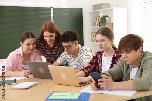 Obraz na płótnie Group of students studying with laptops and notebooks at wooden desk in classroo