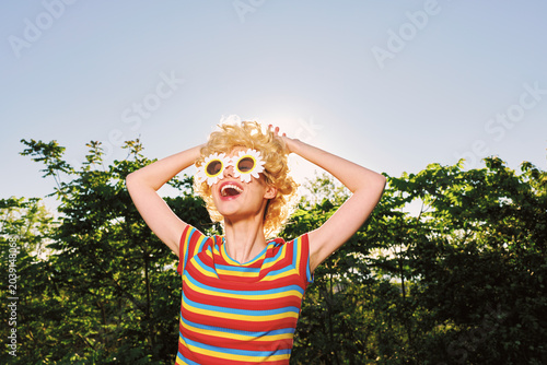 Canvas Print Smiling woman with curly hair wearing flower glasses and a striped shirt in bright sunlight