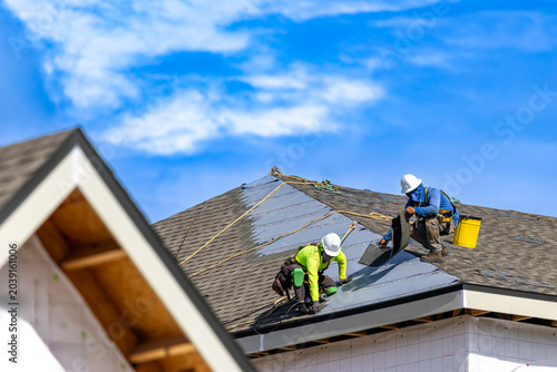 Tableau sur toile A wide horizontal view of two roofers wearing hard hats and safety harnesses whi