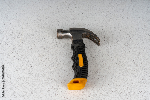 фотографія Small stubby claw hammer tool with a short black and yellow rubberized handle, standing on a light speckled countertop