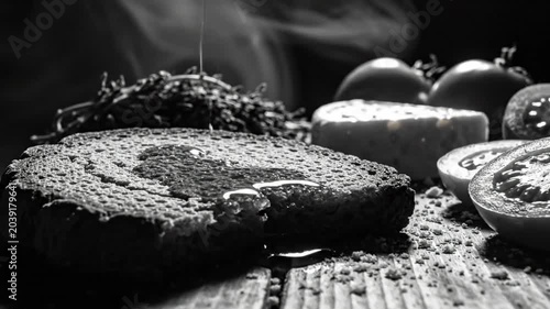 Black and white close up of food, pouring liquid on bread, with tomatoes, cheese and thyme