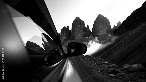 Black and white view from a car driving along a mountain road with majestic peaks and dramatic clouds