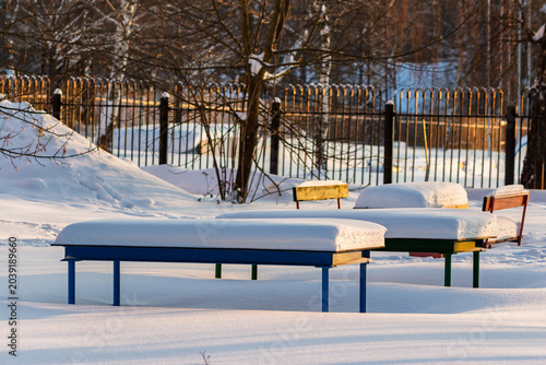Fotografia Cozy park benches and tables topped with thick snow caps, basking in warm golden