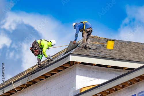 Quadro su tela A wide horizontal view of two roofers wearing hard hats and safety harnesses whi