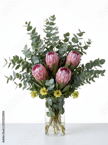 A stunning large bouquet of pink proteas and eucalyptus in a clear glass vase on a white surface