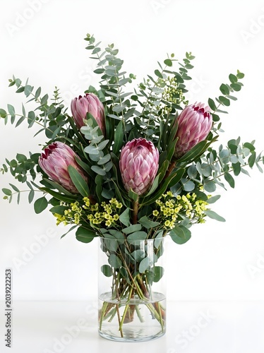 Elegant bouquet of pink protea flowers and eucalyptus leaves in a clear glass vase against a white background
