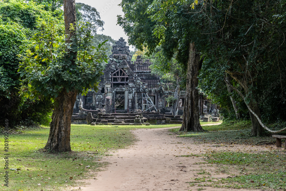Fototapeta premium The ancient stone ruins of Banteay Kdei temple in Siem Reap, Cambodia, are overgrown with lush green jungle foliage, showcasing its historical significance.