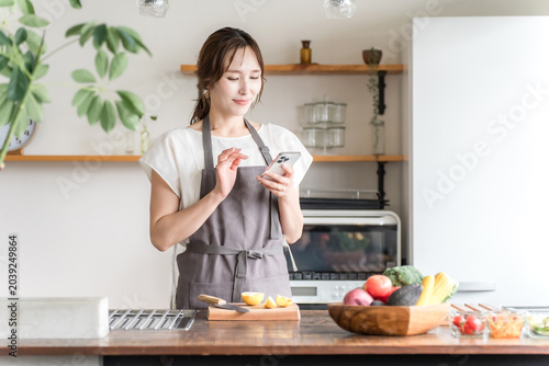 An Asian woman using a smartphone app in her kitchen/dining room at home.