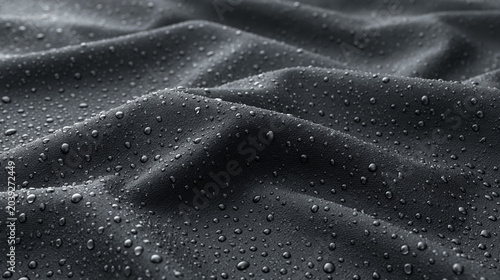 Close-up of dark fabric with water droplets reflecting light in abstract patterns, emphasizing texture and a sense of cool moisture