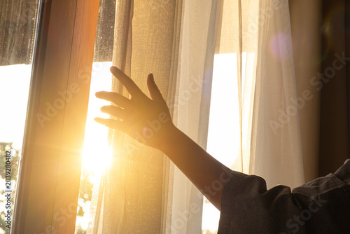 woman's hand She opened the curtains on the window. There was morning light through the window in her room, looking at the view of the mountains and trees as the sun rose	