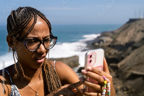 Tableau sur toile Young woman concentrating on phone screen by sea