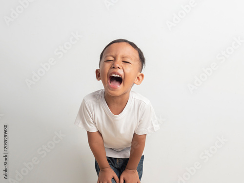 Adorable young asian boy wearing a simple white shirt showing a wide happy toothy smile while looking directly at the camera in this bright studio portrait photograph for your project
