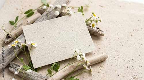 A minimalist stationery mockup featuring an empty recycled paper card decorated with small flowers and natural wood elements.