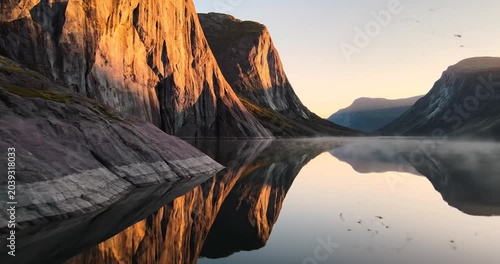 Serene mountain landscape at sunrise reflecting in calm lake with misty background