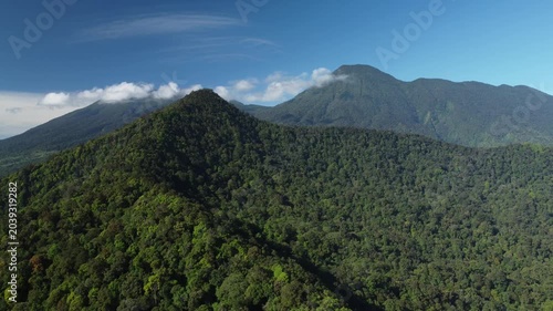 Cinematic drone footage capturing a panoramic view of Mount Gede and Mount Pangrango. The camera moves in a smooth forward and sideway tracking shot over the lush green rainforest canopy. Clean enviro