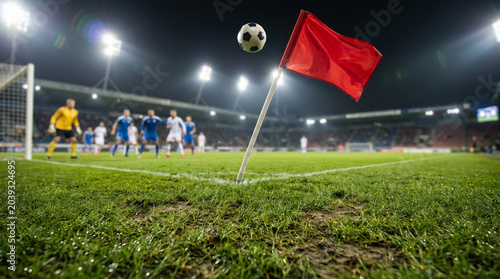 Dramatic soccer corner kick under stadium lights with red flag in foreground and players poised for action on lush green field