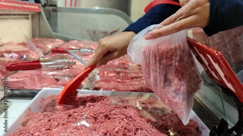 An unrecognisable woman uses a scoop to transfer fresh ground beef into a plastic bag, carefully packaging the meat for purchase at a market or supermarket.