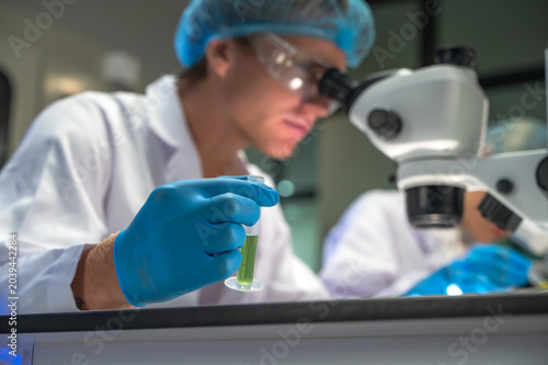 Focused male scientist wearing lab coat intently conducting research on epidemic strain using binocular microscope in  well equipped biomedical laboratory
