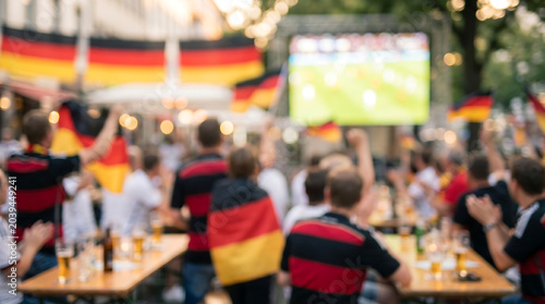 Intentionally blurred view of German soccer fans gathered at a public outdoor screening to watch a football match for editorial backgrounds, social media graphics, and event marketing.