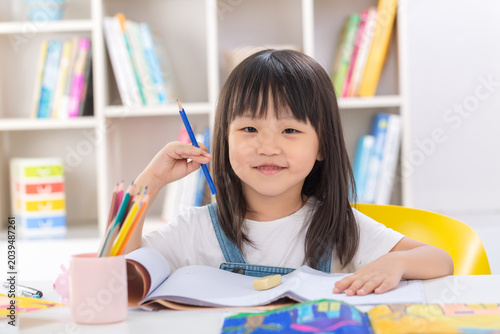 Bilde på lerret A polite and happy little Asian girl sitting up straight at her desk with crossed arms and smiling brightly at the camera