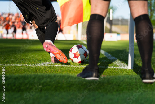 Foto Low angle shot of a soccer player kicking a ball from a corner with a referee's flag and legs in the foreground