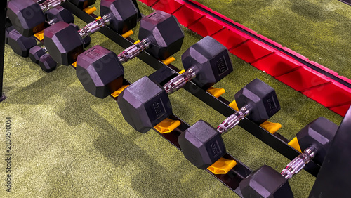 Photos Black dumbbells of various weights on a rack in a modern fitness room with bright lighting and a sporty interior