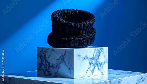 Dark blue knitted scarf or cowl displayed on a marble pedestal against a vibrant blue background with dramatic lighting
