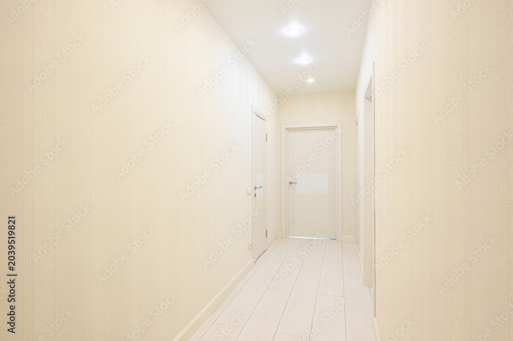 Fototapeta premium narrow hallway with cream-textured walls, white tiled floor, recessed ceiling lights, and three closed white interior doors along the sides