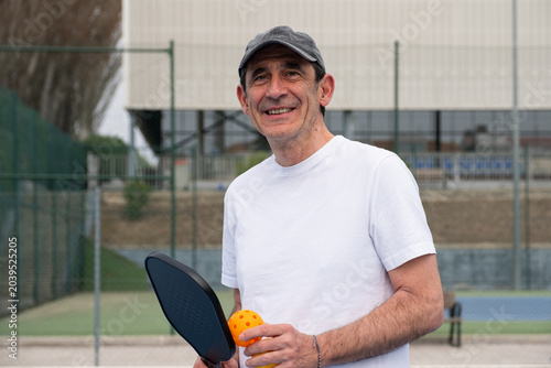Senior man smiling outdoors ready for a pickleball game on the court