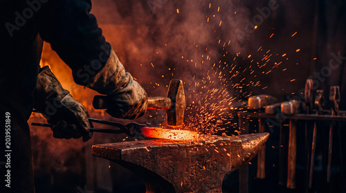 Canvastavla Strong blacksmith in leather gloves hammering glowing hot metal on an anvil, creating a shower of fiery sparks