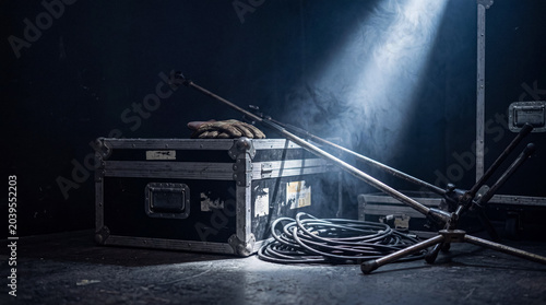 Konstfotografi Stage equipment: a flight case, microphone stands, coiled cables, and gloves on a smoky, dark stage floor