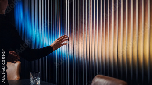 Obraz na plátne A human hand touching a sleek modern vertical slatted wall illuminated with vibrant colorful light