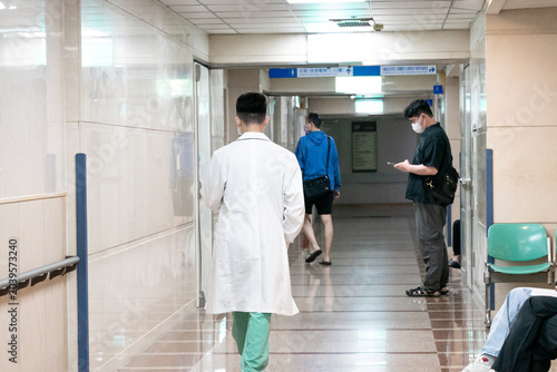 Photos A physician walks through a bright hospital corridor, captured from behind to emphasize professionalism and daily medical responsibilities