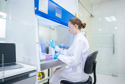 Scientist working in a sterile laboratory fume hood with pipettes and samples