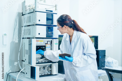 Scientist in lab coat and gloves operates advanced chromatography equipment for analysis
