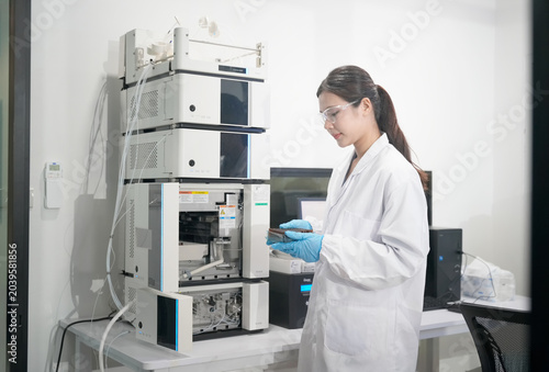 Scientist in lab coat and gloves examines samples near advanced chromatography equipment
