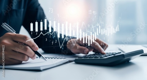 Financial analyst using calculator and notebook with stock market data graph overlay on desk with laptop and documents for business analytics and accounting concept