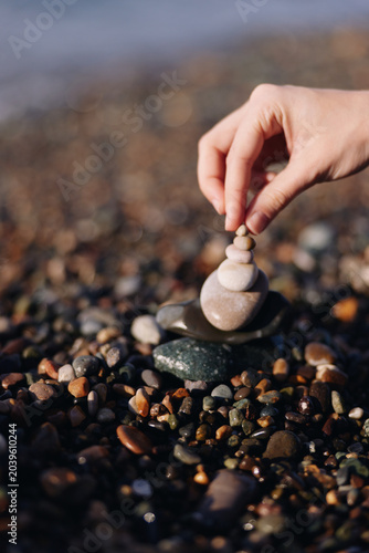 Photography Stones balance on a pebble beach as a hand carefully stacks a small cairn, creating a zen moment of calm, focus, and natural sculpture amid smooth rocks and coastal sand