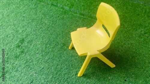 Bright yellow miniature plastic chair on a textured green artificial turf background.