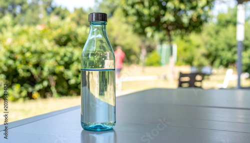 Εκτύπωση καμβά Refillable glass water bottle on outdoor table in summer light, creating refresh