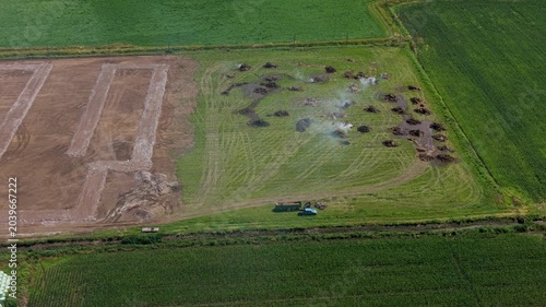 Aerial drone view of burning dry grass piles in an open field, natural rural scene, daytime.